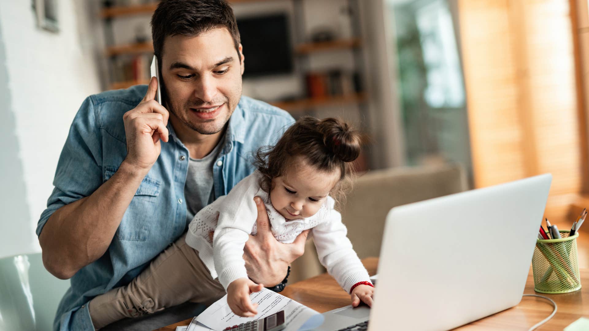 Busy man holding his baby and talking on the phone.