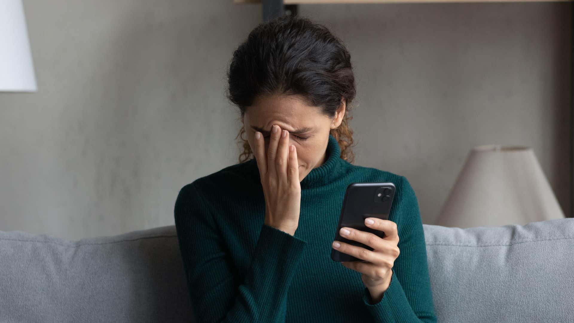 woman in green sweater doesn't feel heard as she puts head in hand and holds phone clearly upset