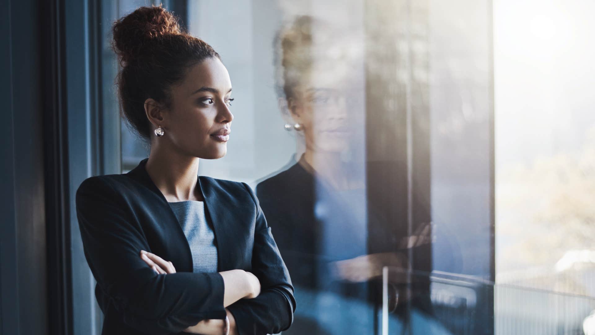 woman in black jacket has evolved as she looks out the window with her arms crossed