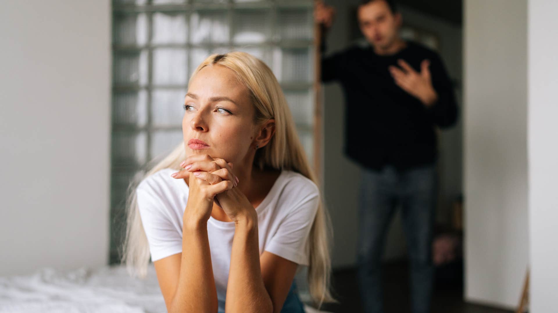 woman in white shirt tired of feeling like a roommate as she looks over to the side and husband tries talking to her