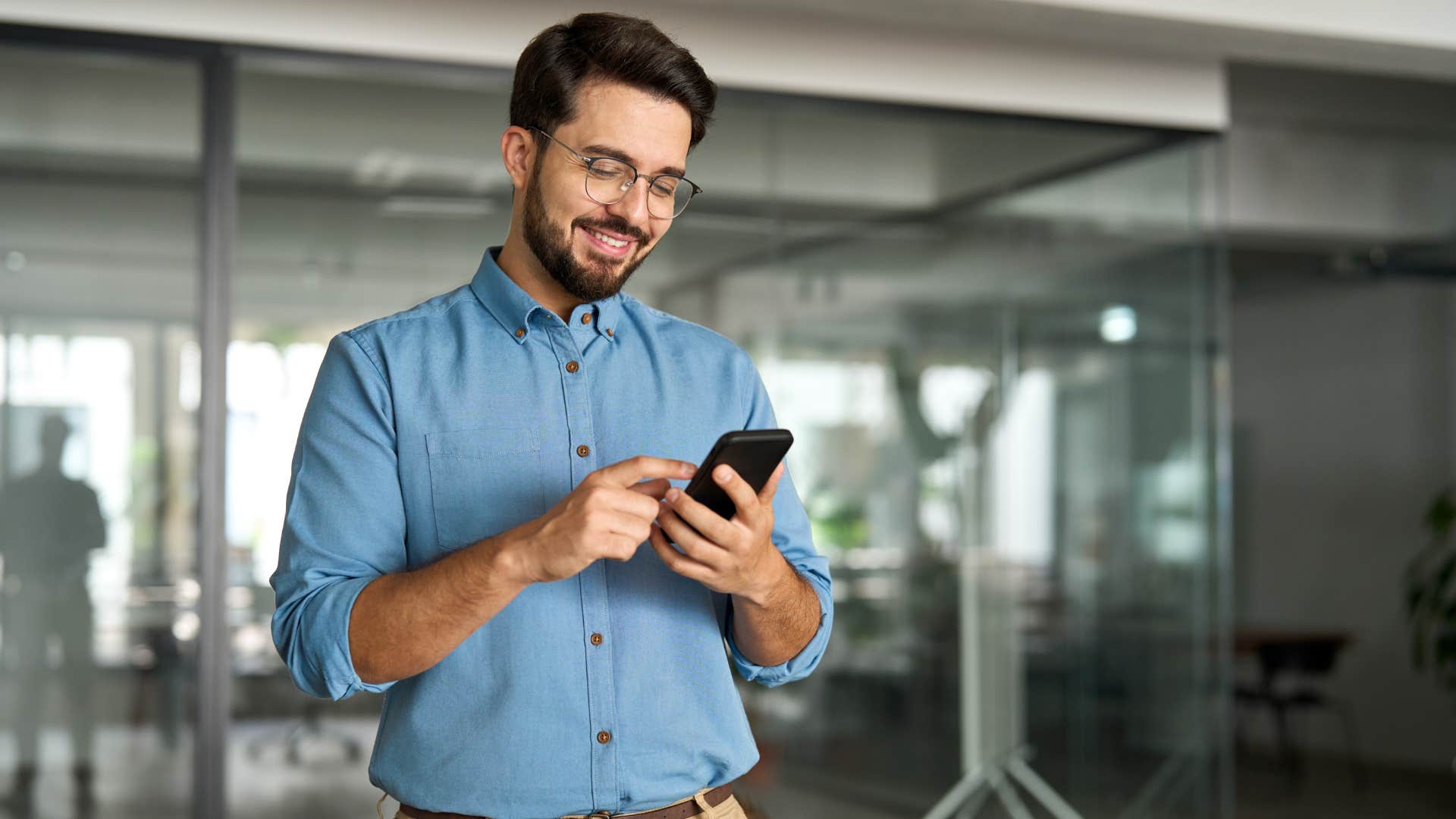 man in blue shirt always buying the new iphone as he scrolls through iphone while smiling