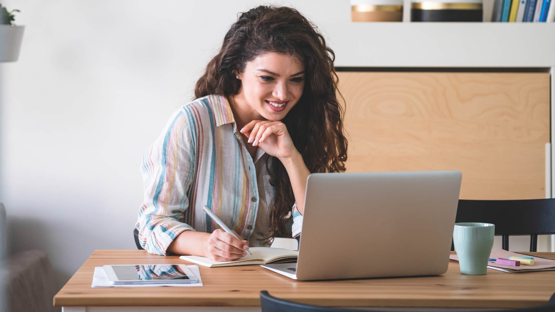 woman writing with pens staring at laptop