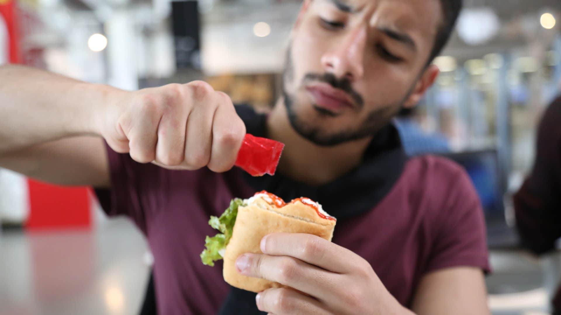man using a ketchup takeout condiment on his burger