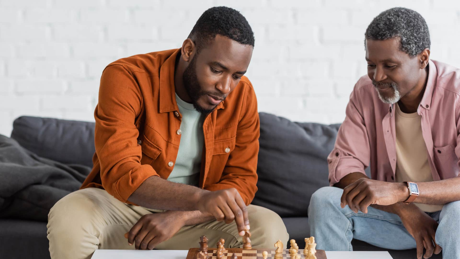 two men playing chess on dark couch