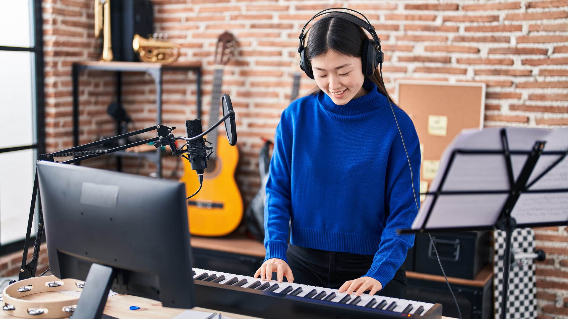 woman in blue shirt playing a musical instrument as she plays on the piano with headphones in