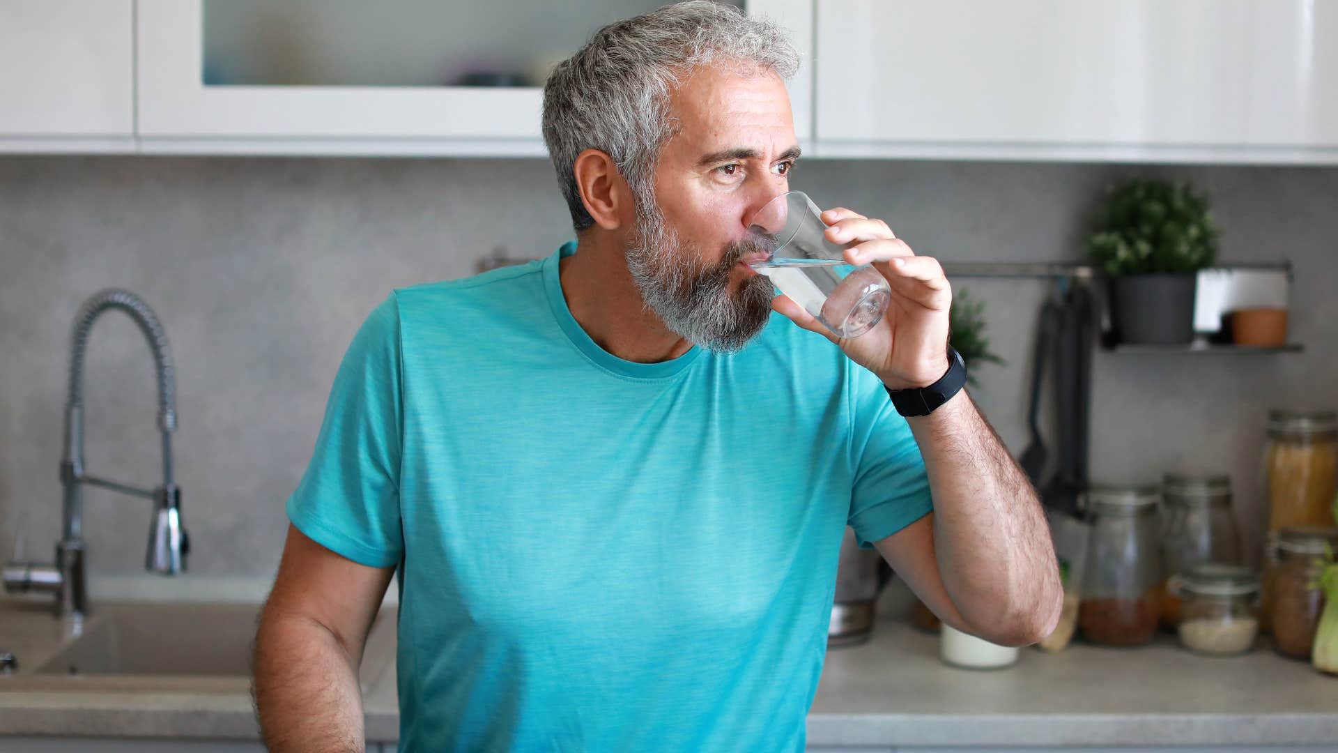 man drinking plenty of water standing in his kitchen