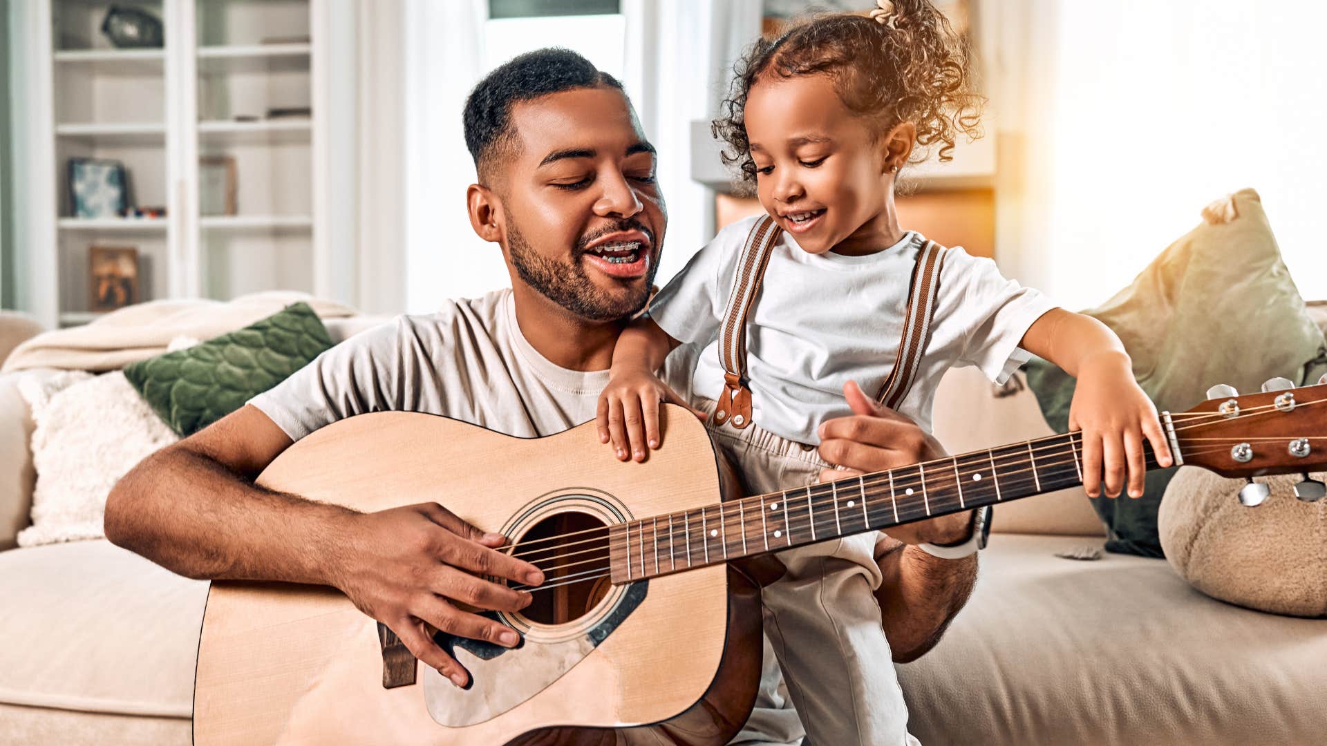 good man playing a guitar at home with his daughter