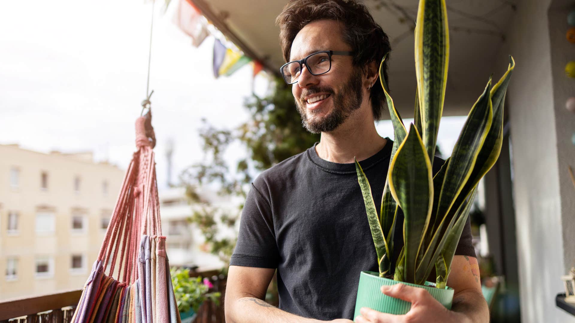 good man holding plants on his balcony and smiling