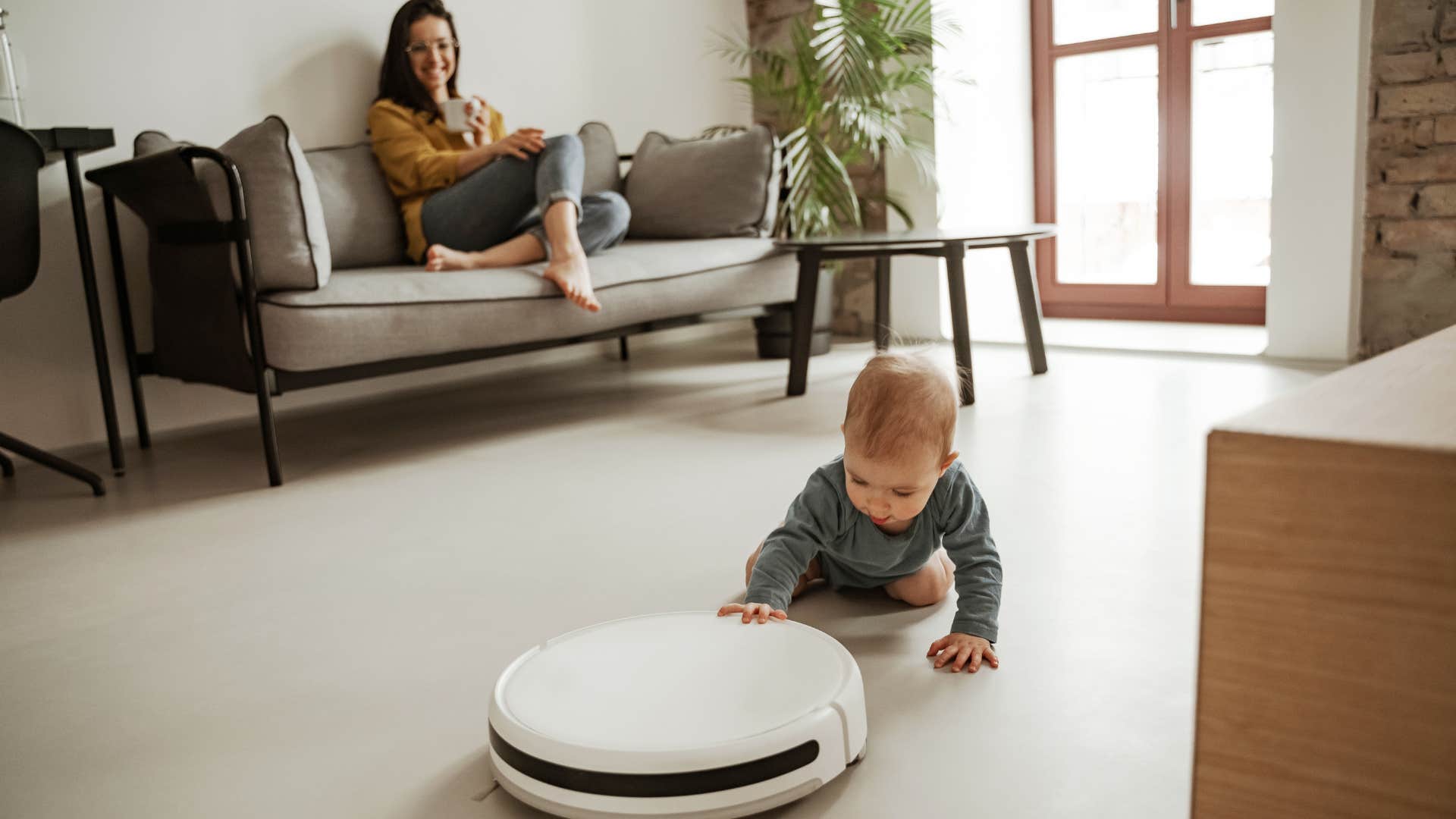 woman watching her infant play with a robot vacuum