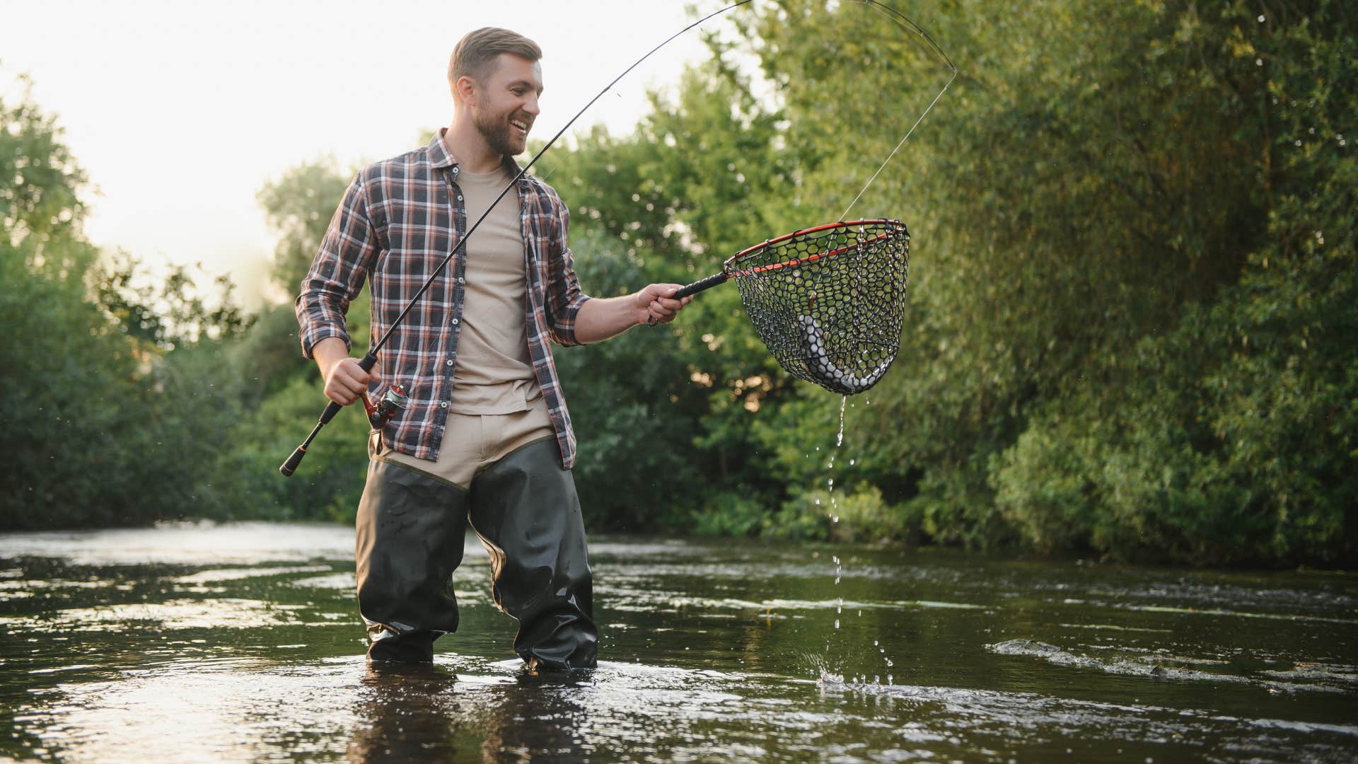 man in plaid shirt with hunting gear as he catches fish with net