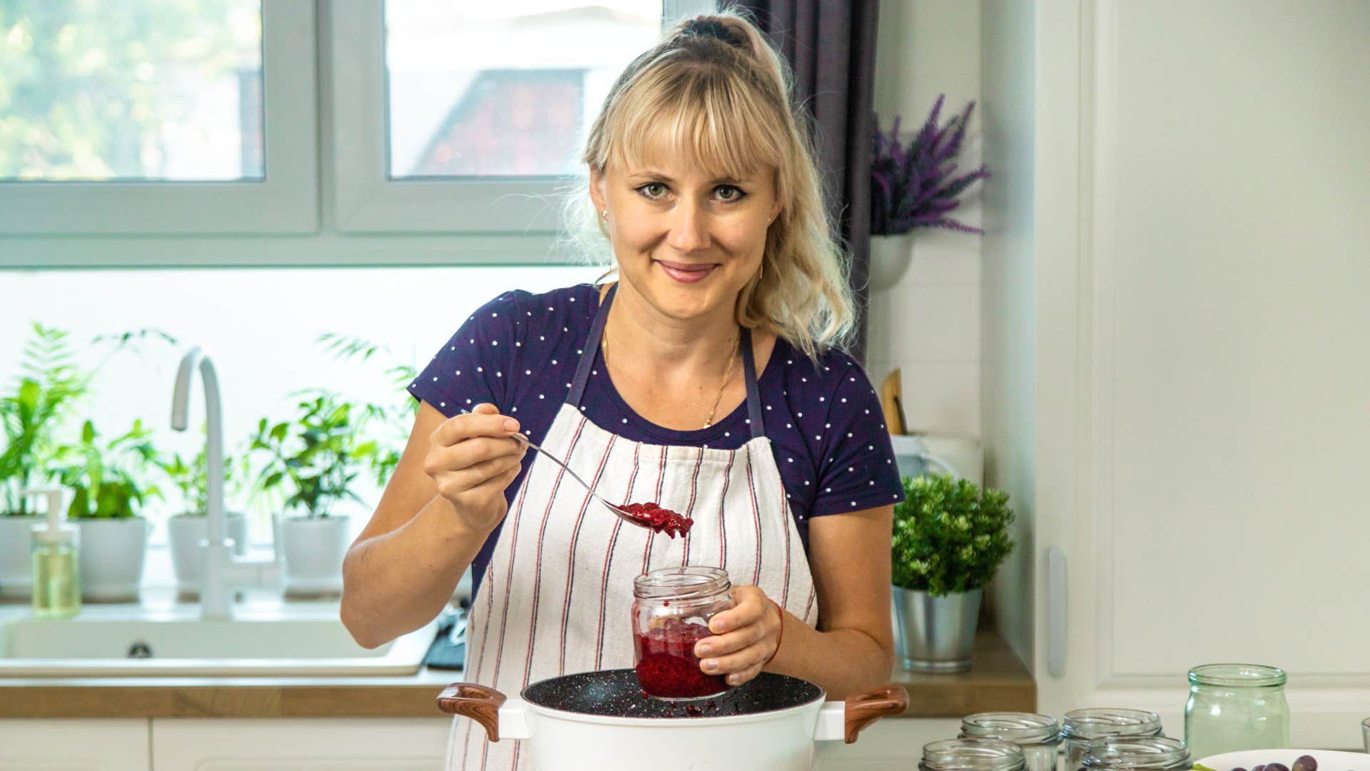 woman in apron canning goods in mason jars while smiling at the camera