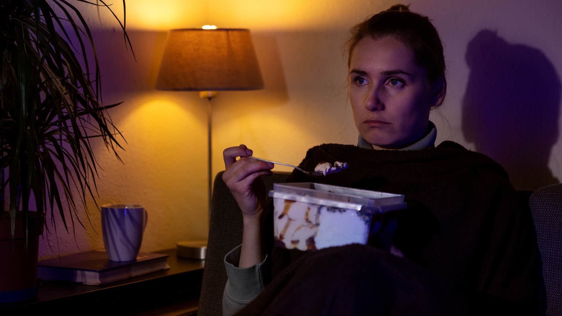 a burned out woman sits in a dimly lit room eating ice cream
