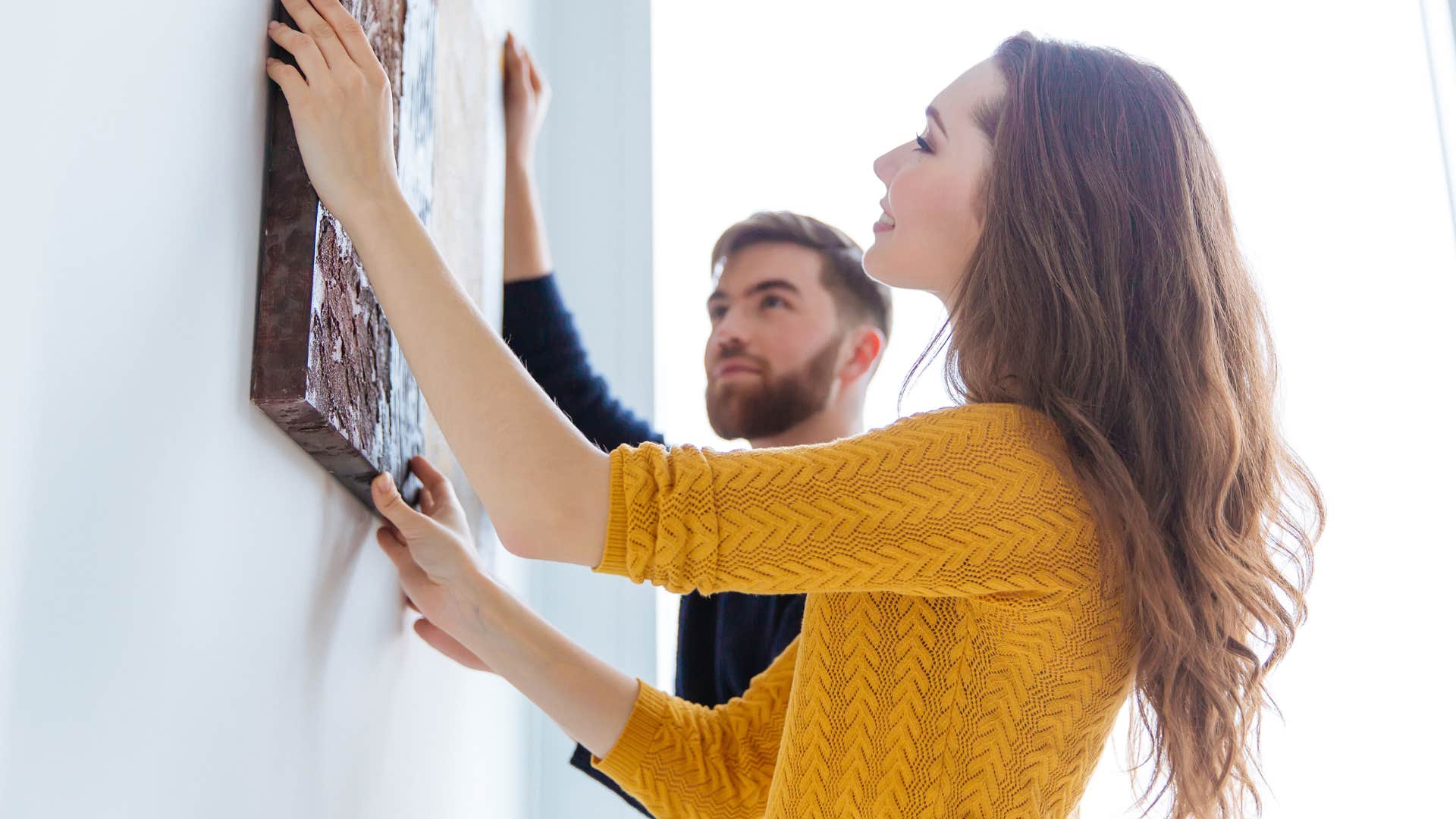 Woman smiling and hanging up inspirational home decor with her partner.