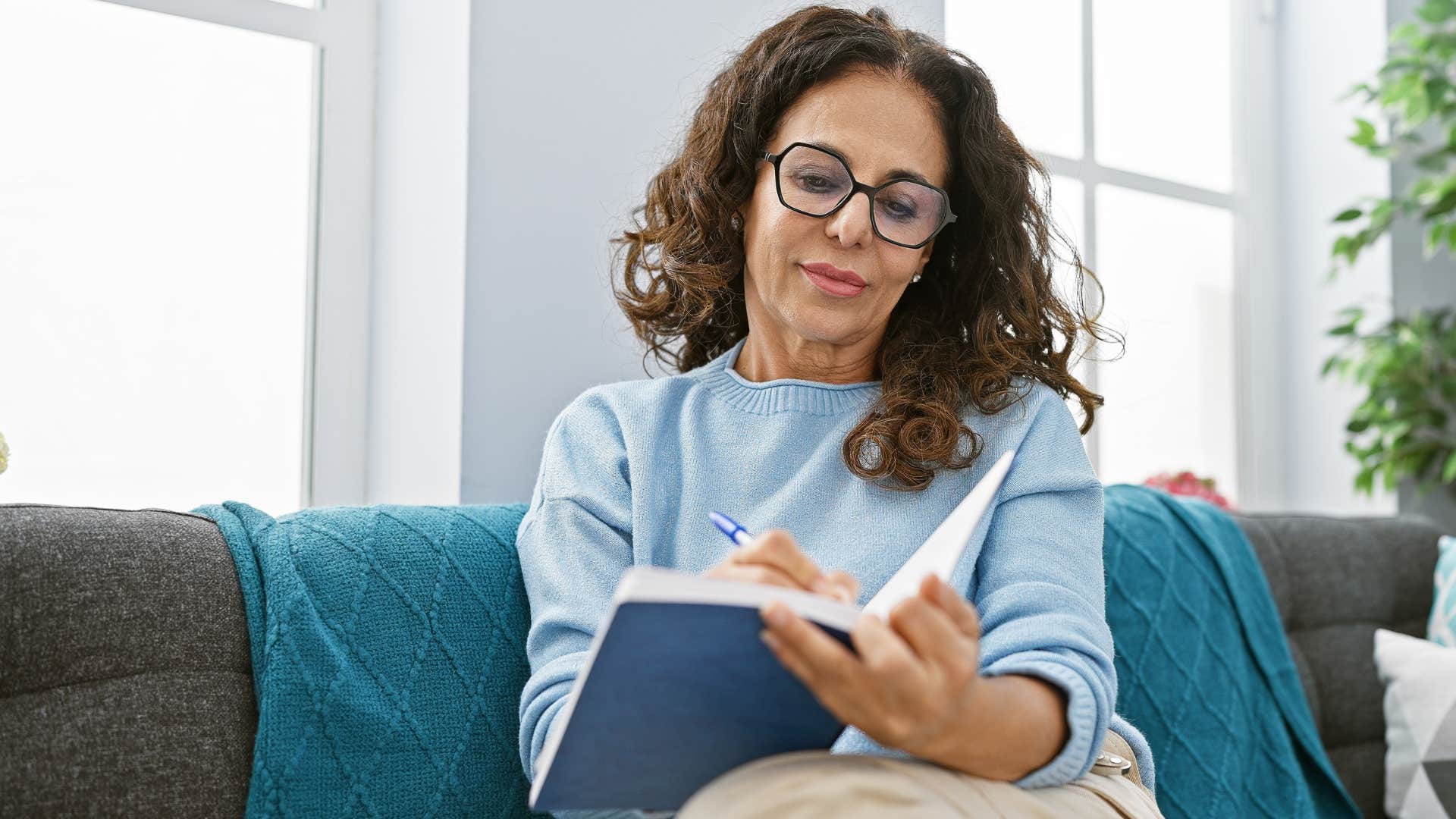 Woman smiling and writing in a well-used journal at home.