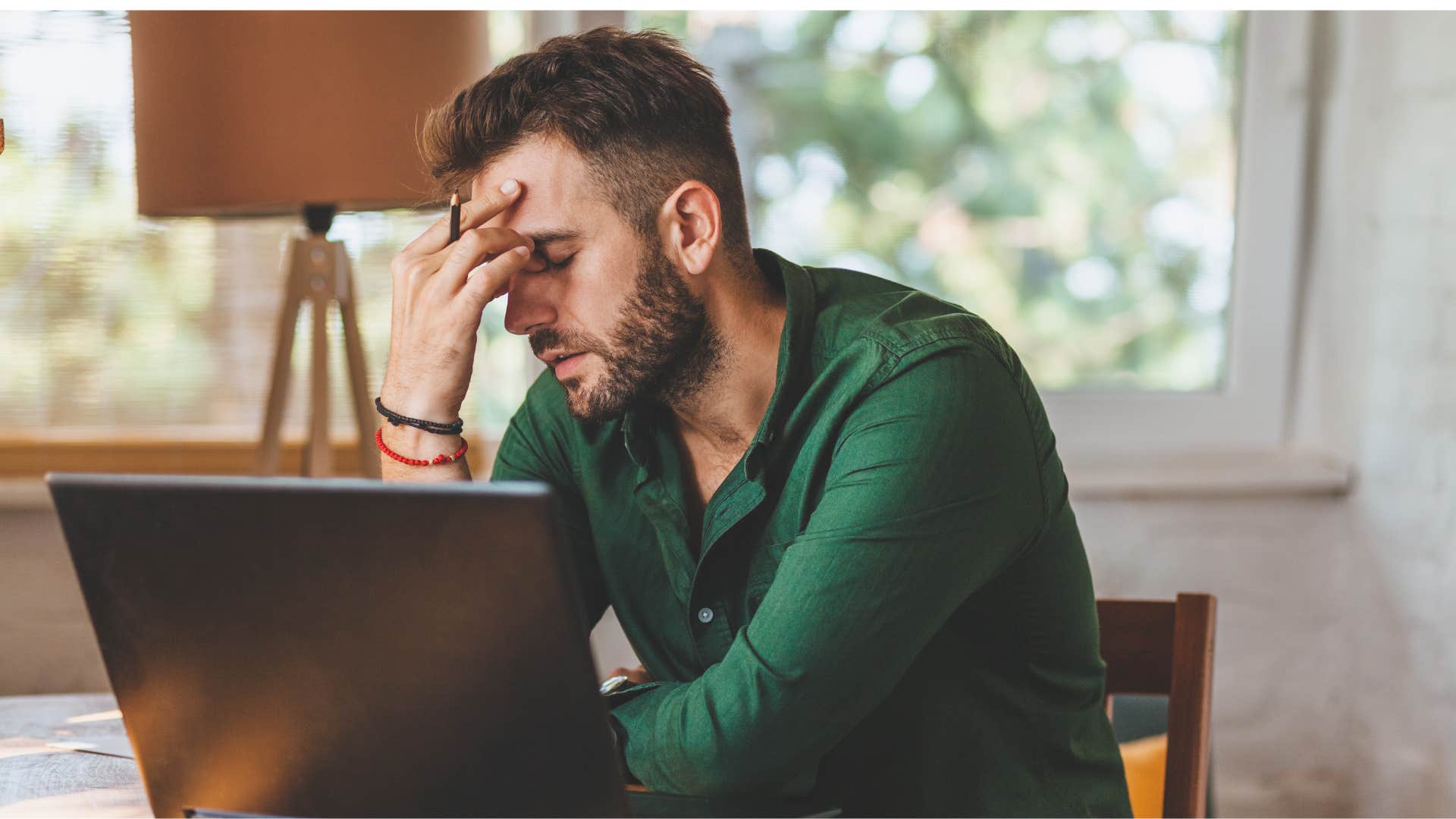 man in green shirt burned out as he puts head in hands 