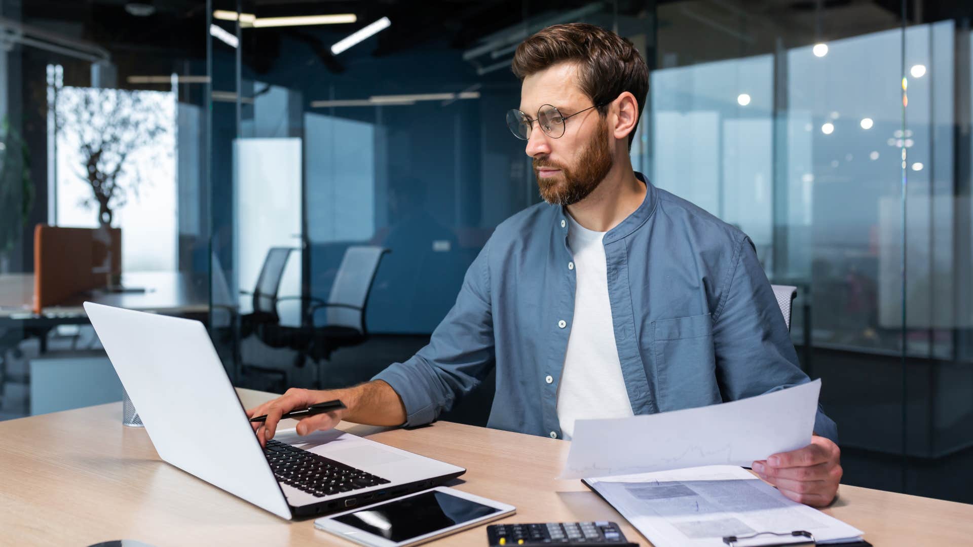 man prioritizing work over relationships as he works on laptop and holds paper