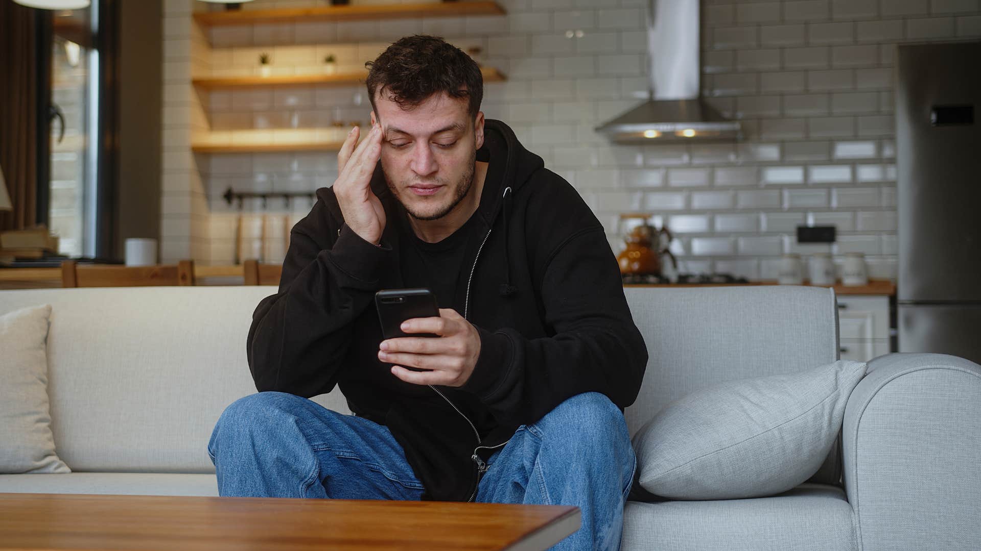 man in black hoodie on phone as he doesn't know how to rekindle old friendships