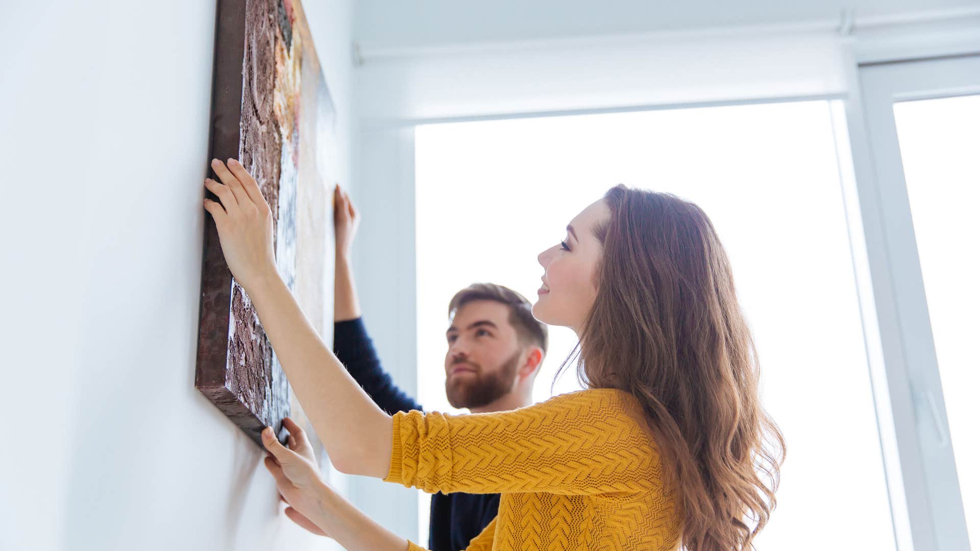 woman in yellow shirt hanging up bold art on wall with help of man