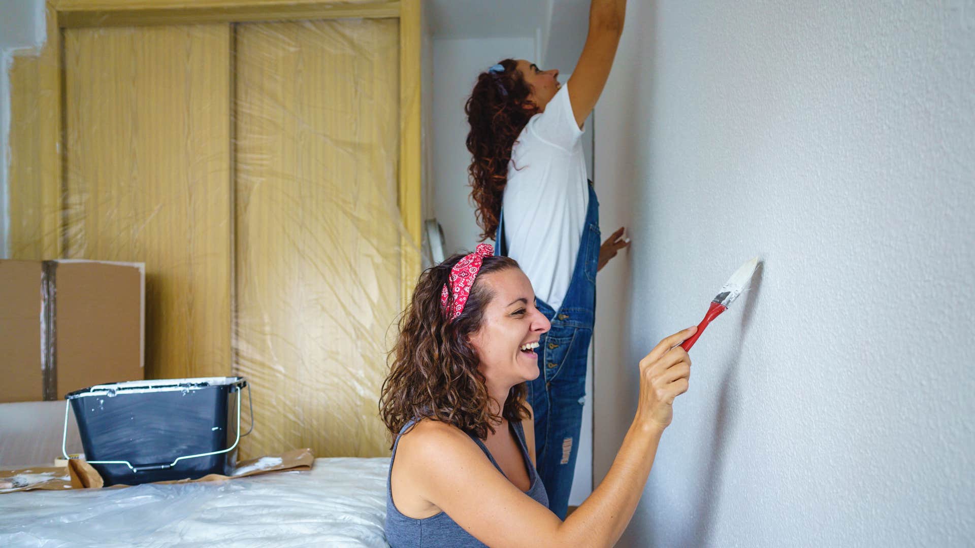 woman with gray t-shirt painting with friend as they draw funny signs on wall