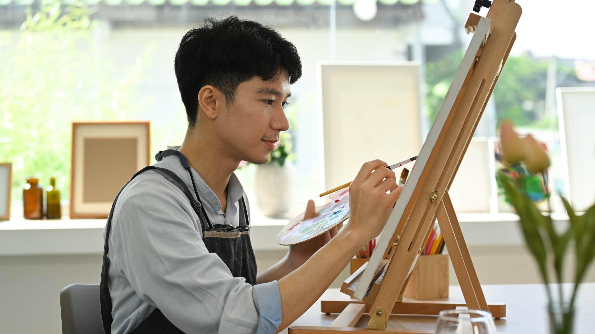 man with apron making homemade diy decor as he sits down and paints