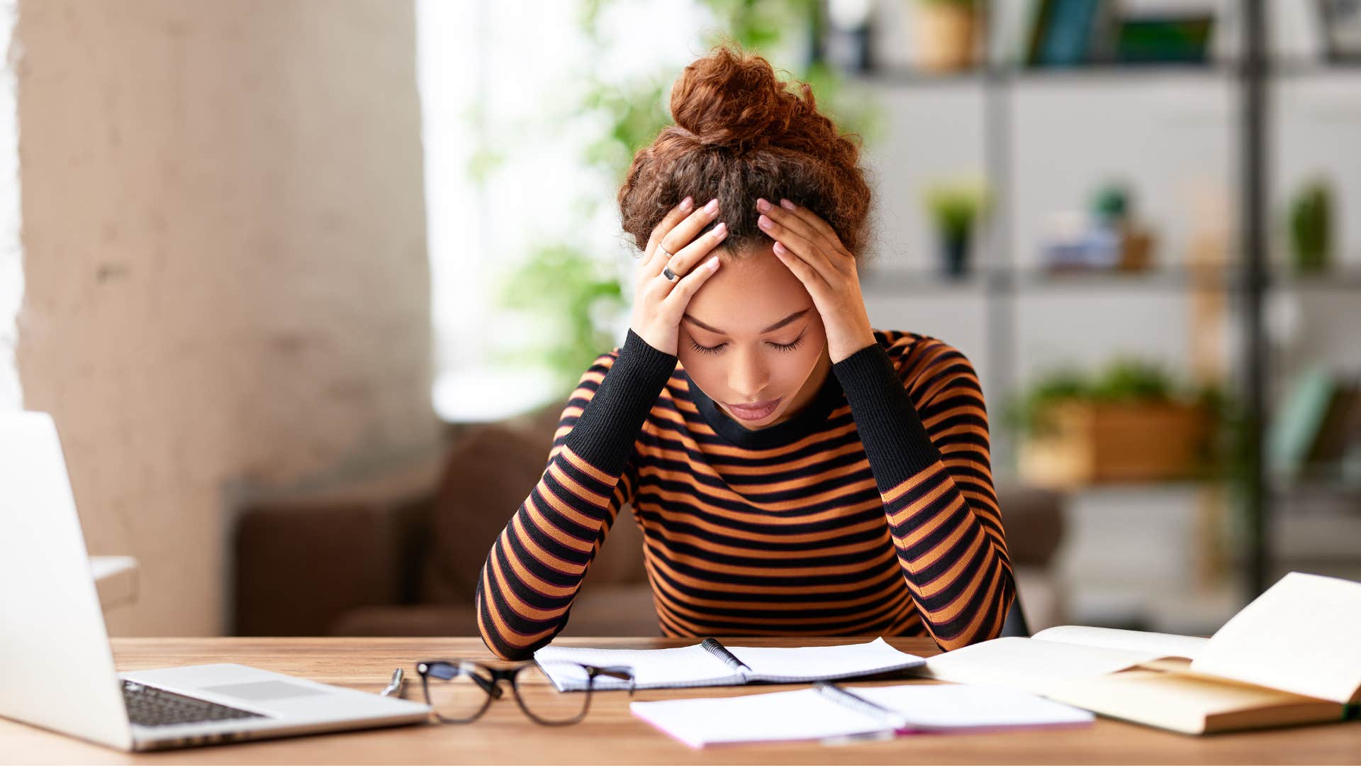 woman in black and orange stripped shirt looking burned out as she puts head in hands in frustration