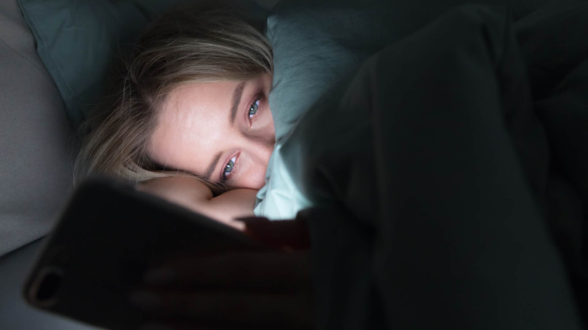 sleepy woman in a dark room texting sorry I was sleeping on her phone