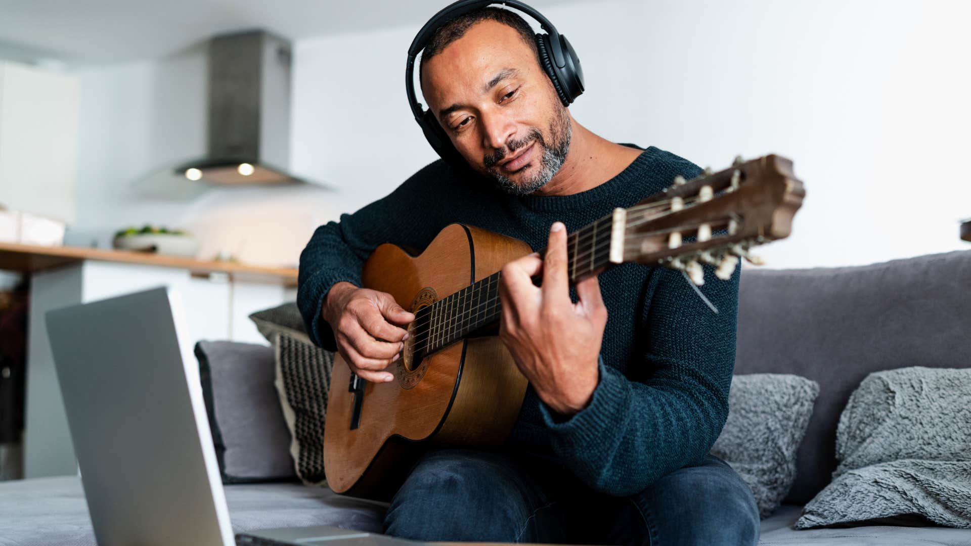 Man with personal interests and hobbies playing guitar at home.