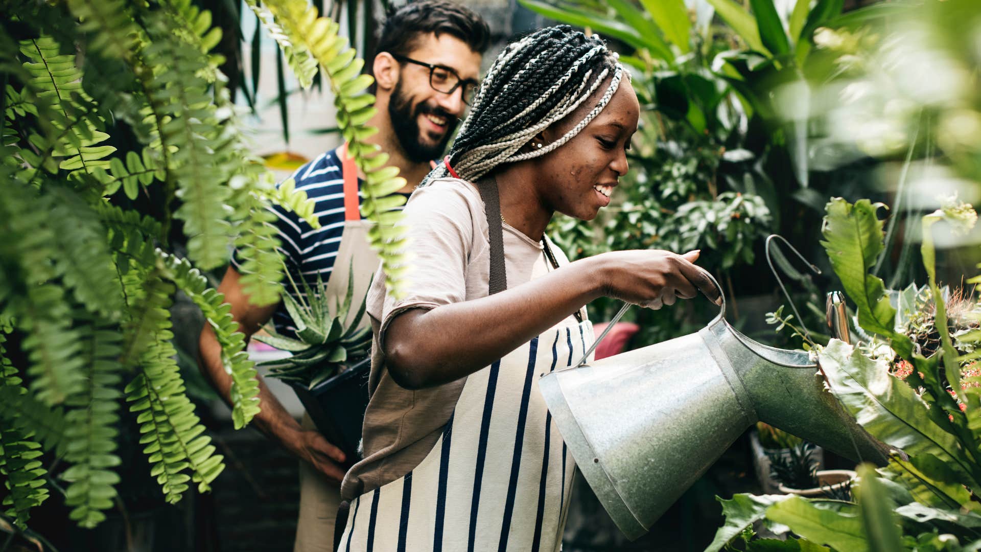 Couple smiling and watering plants together.