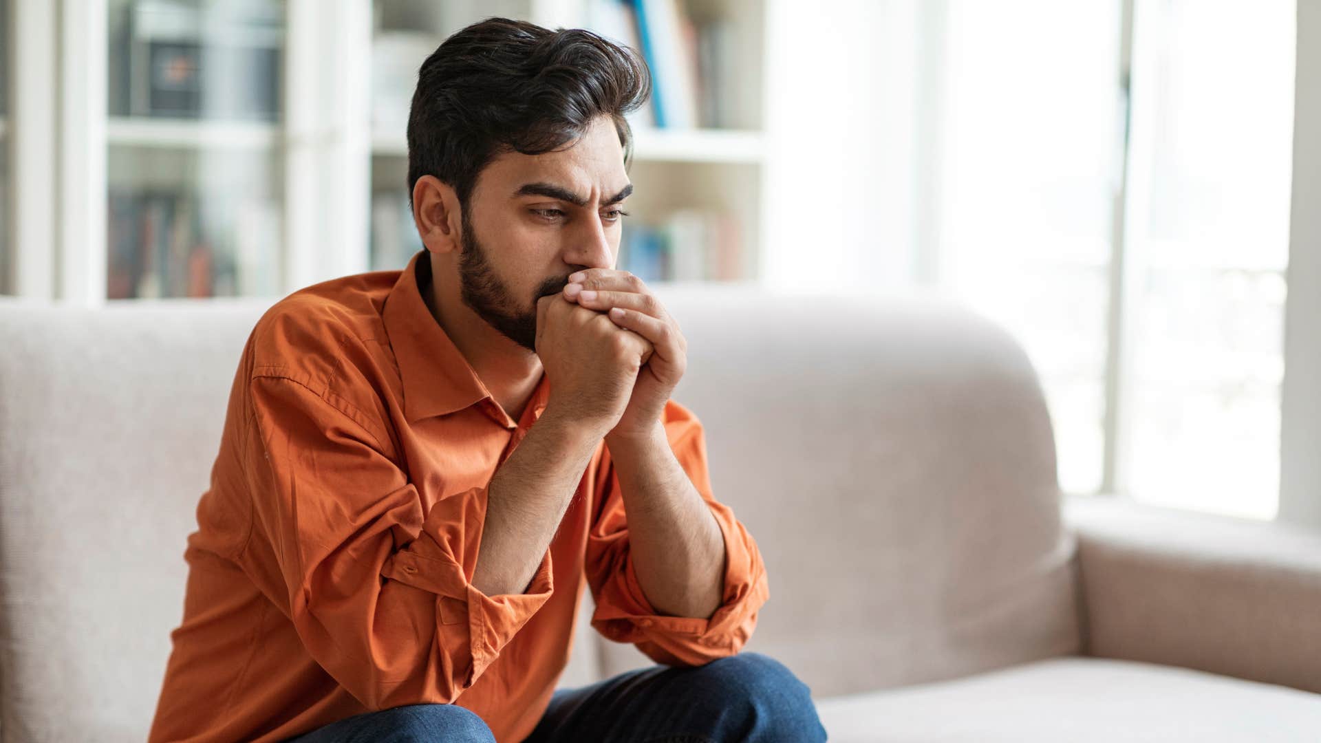 man in orange on the couch thinking looks like i can't do anything right 
