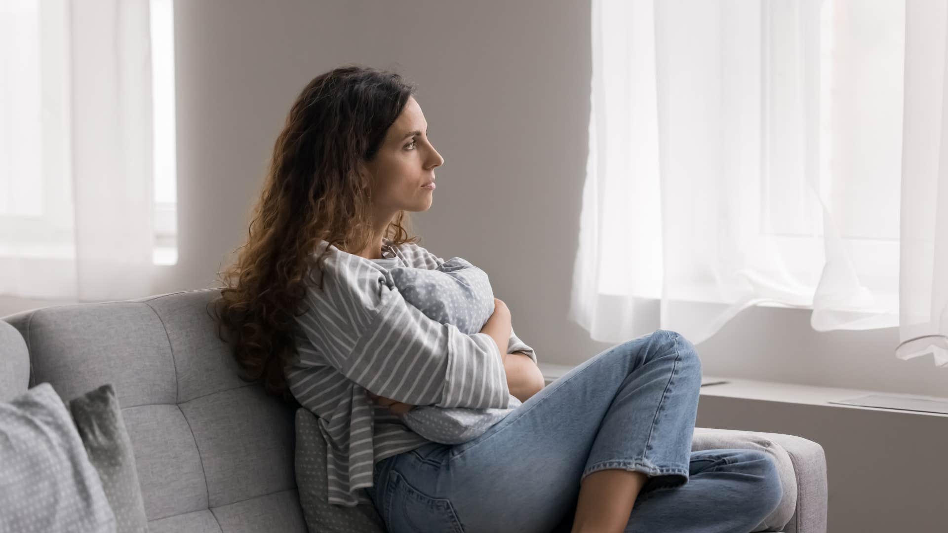 woman in casual attire looking out the window and clutching pillow as she thinks it'll pass
