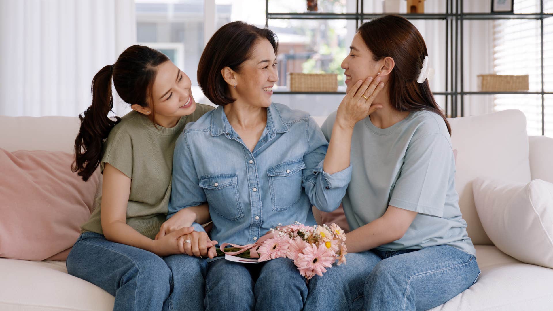 woman in denim shirt having a balanced style of parenting as she cups daughters cheek and other daughter hugs her