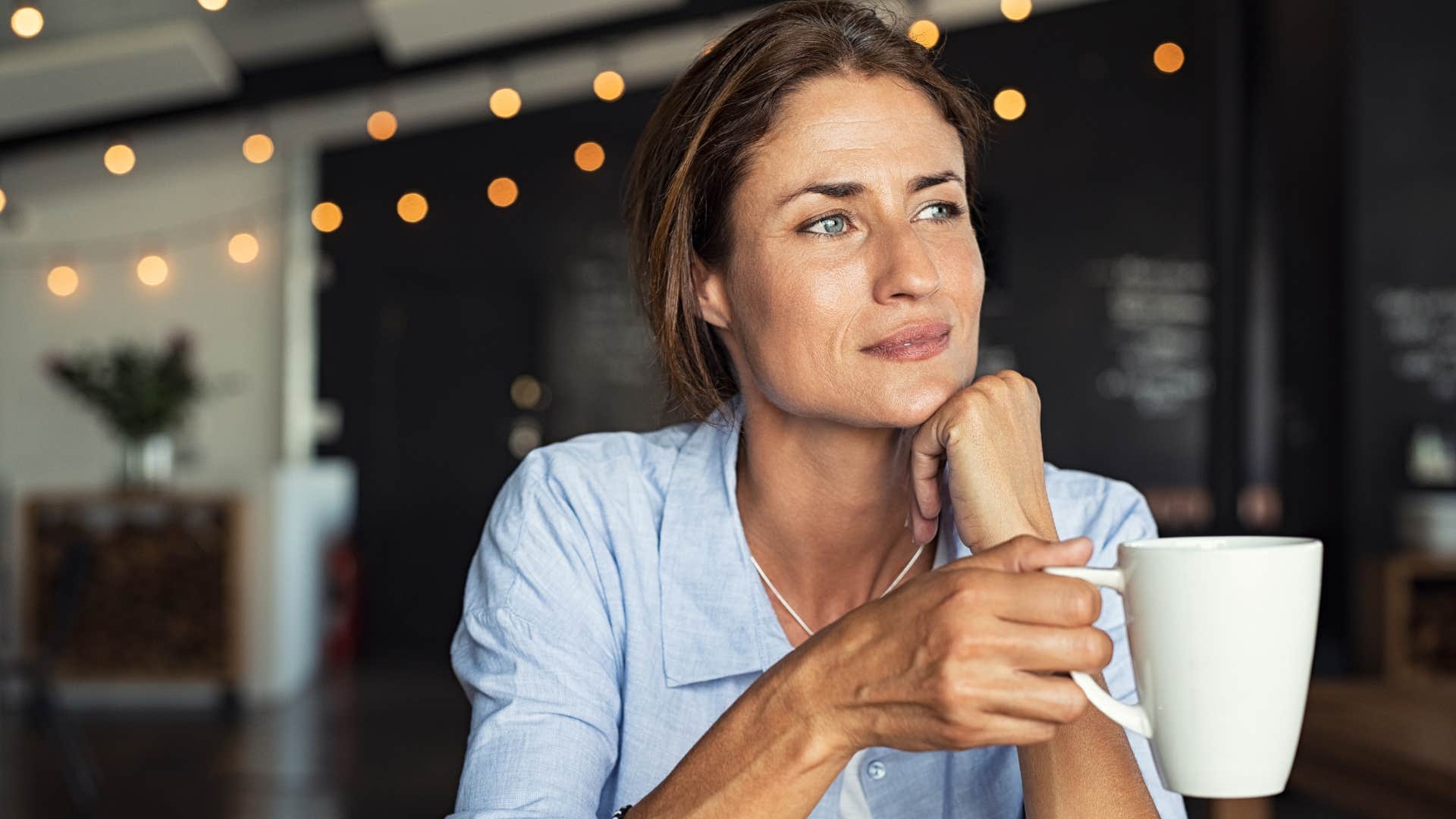 woman in blue shirt with cup of coffee being resistant to cult like trends as she thinks deeply
