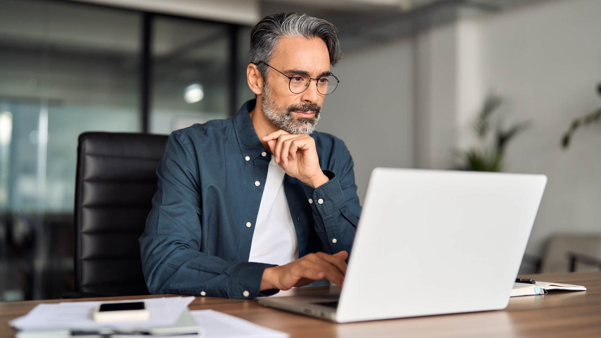 man in white shirt being a skeptical, not cynical thinker as he looks at laptop in deep thought