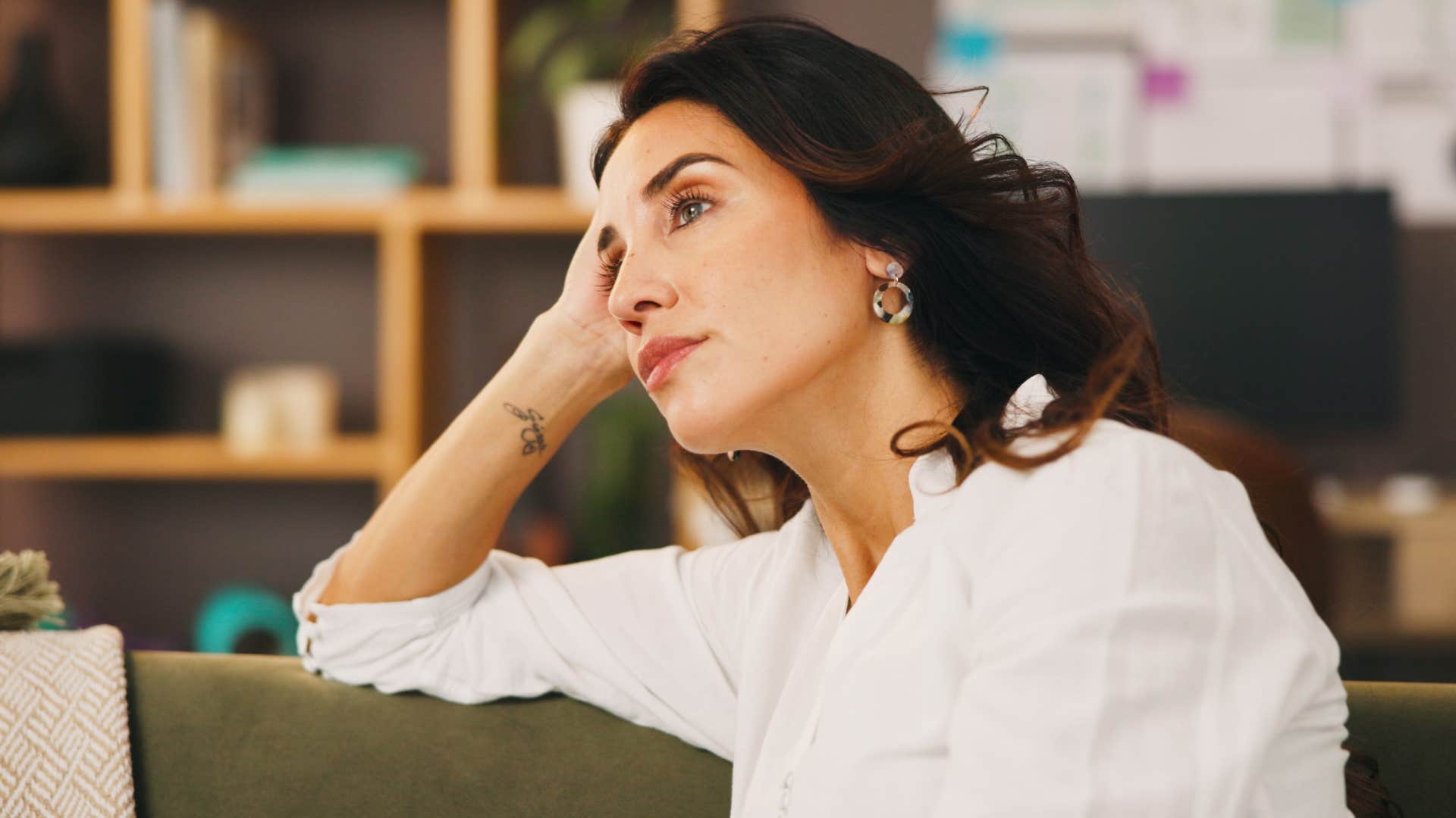 Woman who's a harsh self-critic sitting alone on her couch.