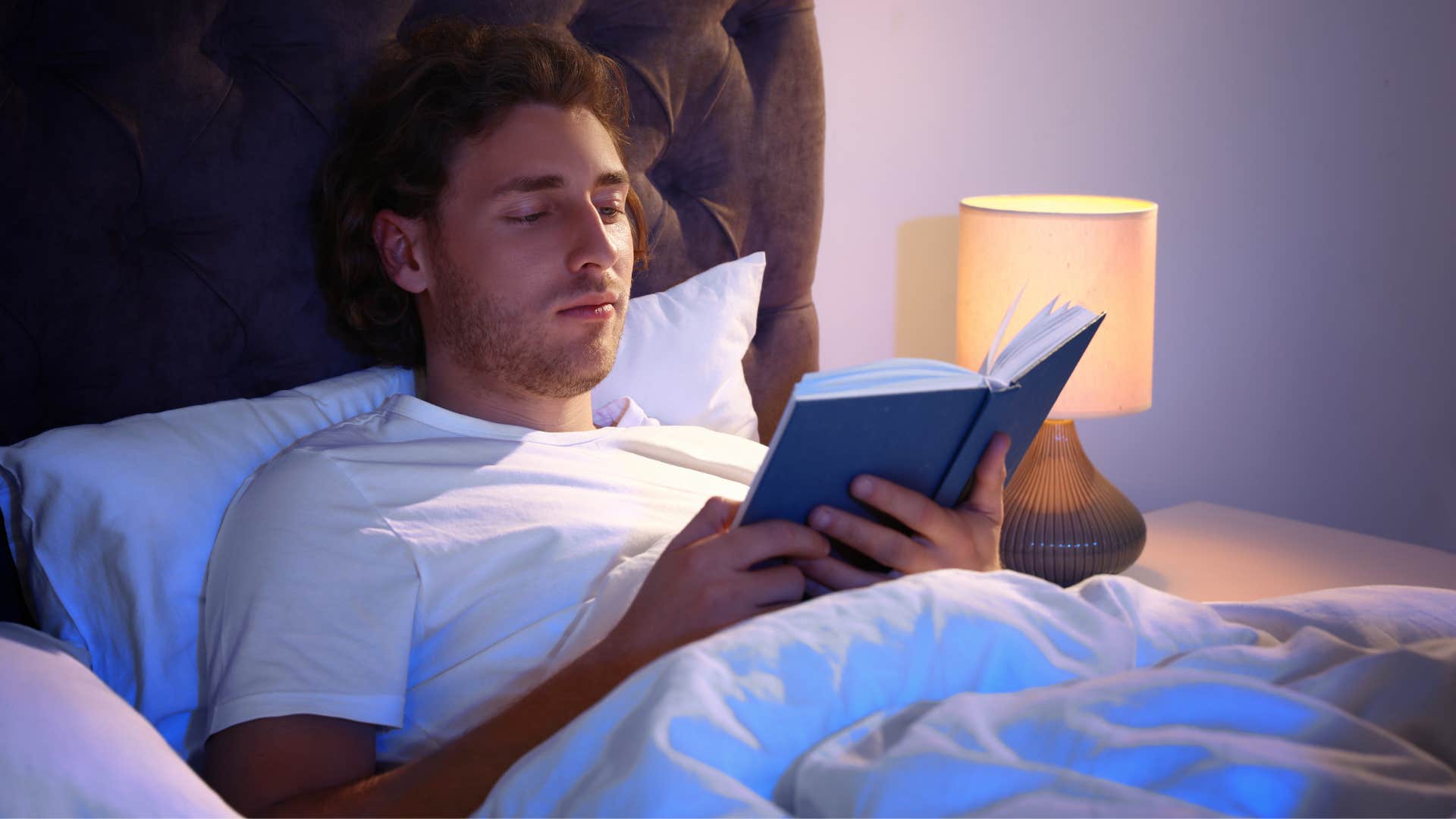 immature man sitting up in bed reading a self-help book