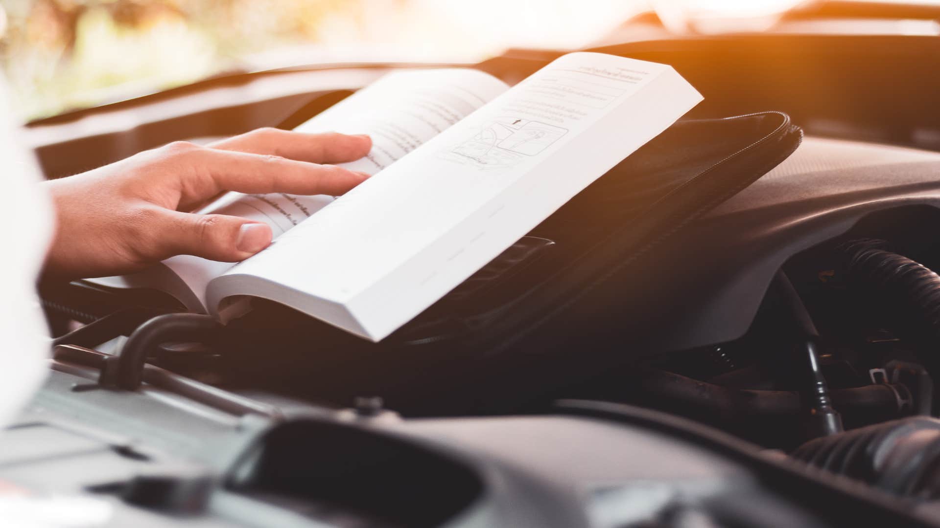 a man reads his cars manual for guidance into fixing something