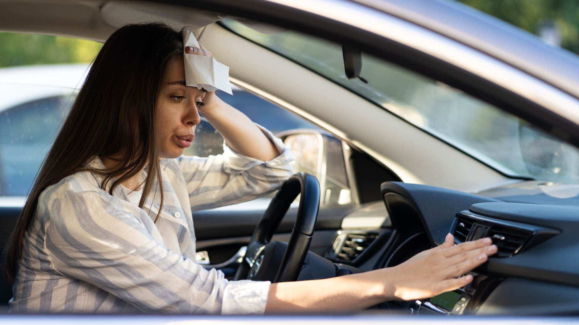 a woman uses the napkins in her car to wipe her sweat as she puts the air on