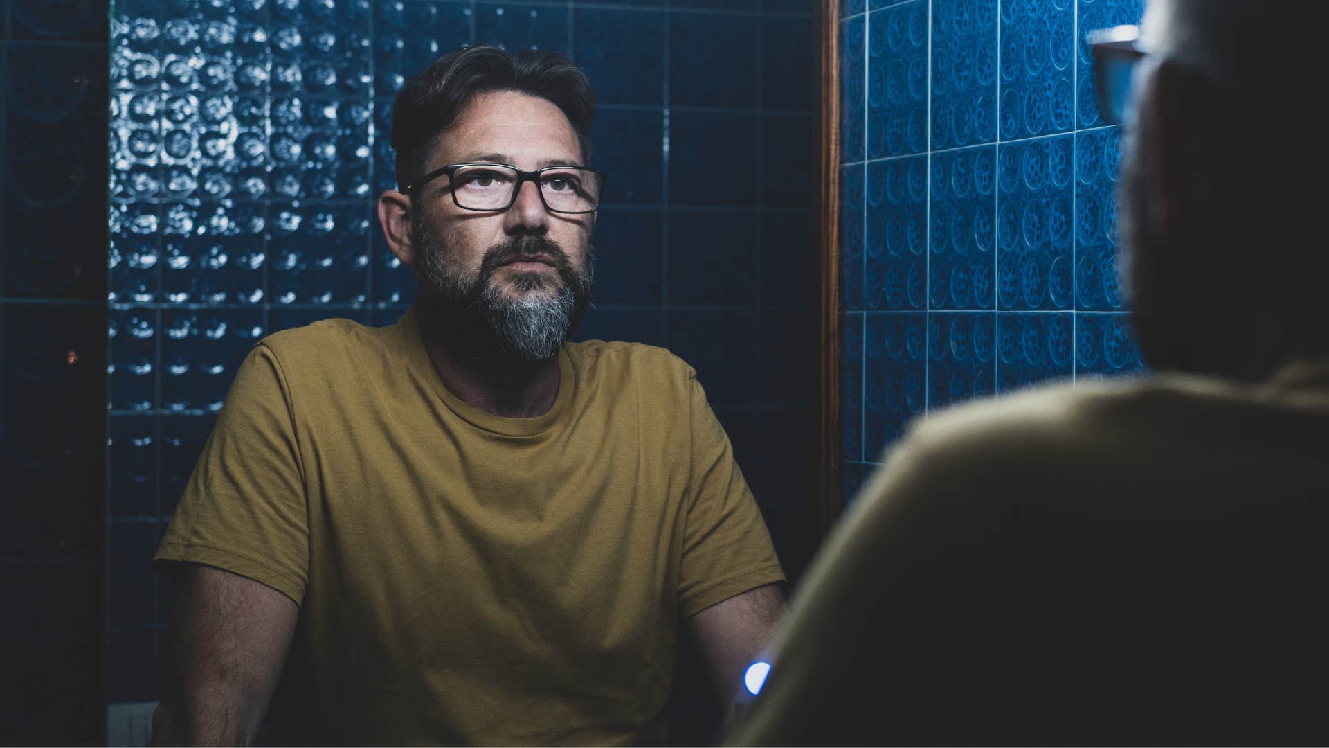 emotionally exhausted man thinking about self-care while looking in a mirror