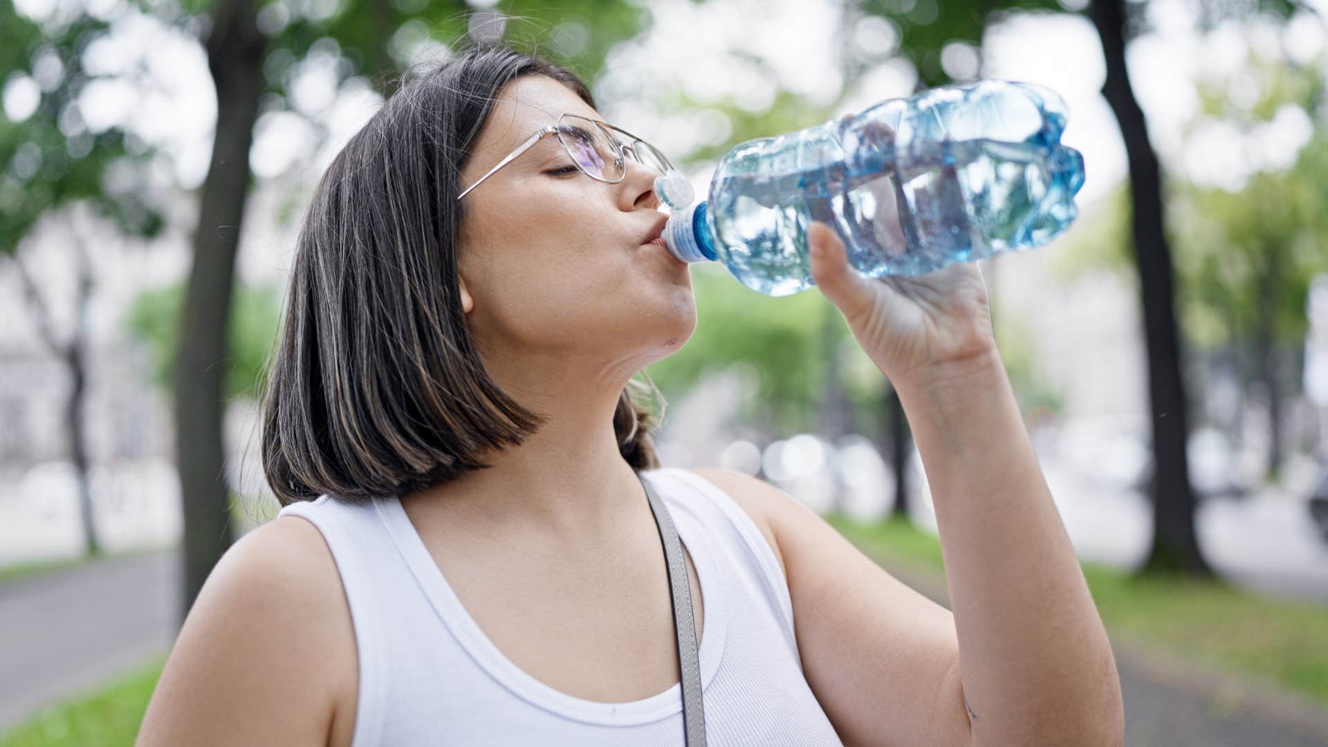 Woman buying bottled water and drinking it on the street.