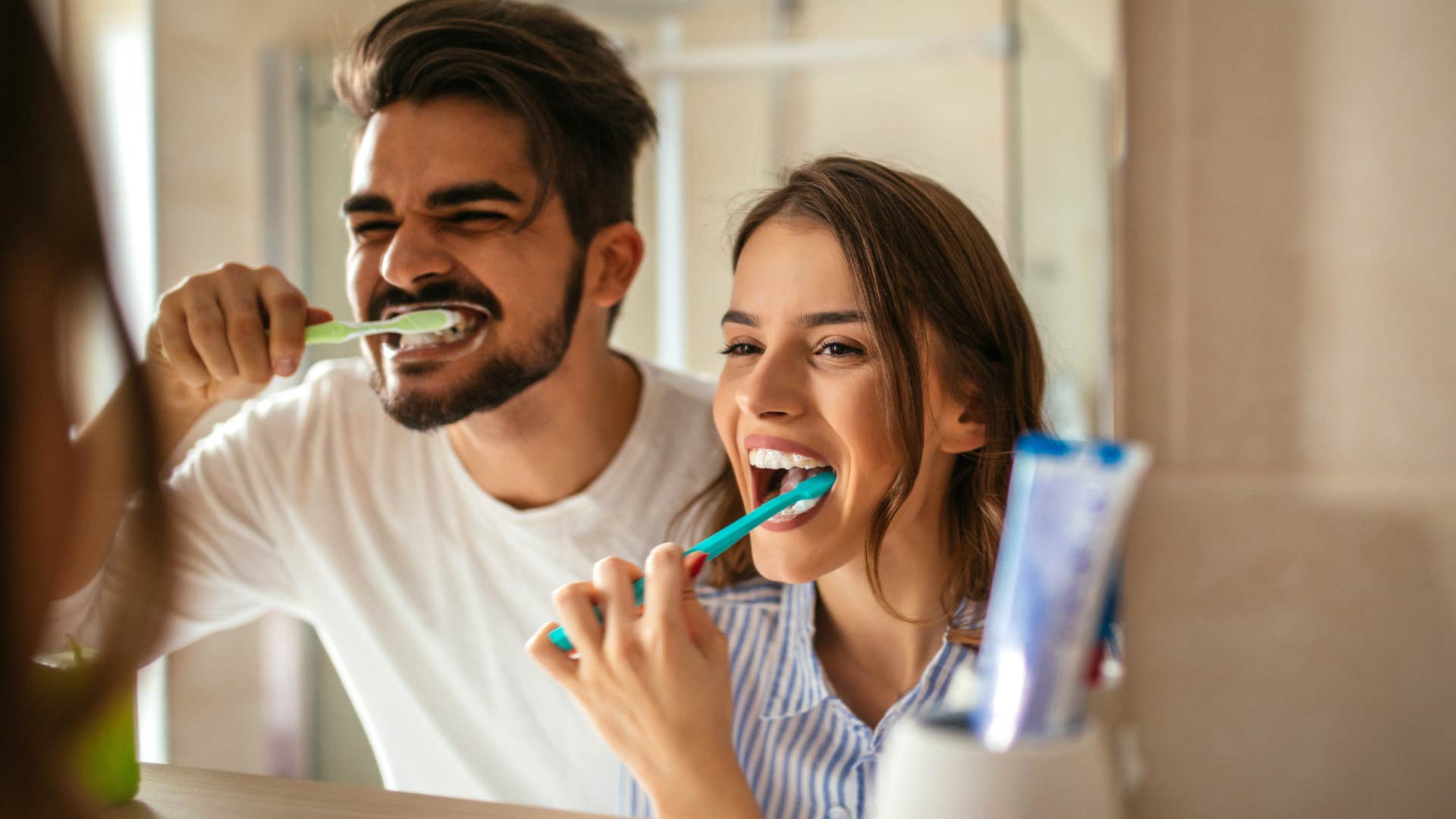 Couple smiling and using hygiene supplies while brushing their teeth.