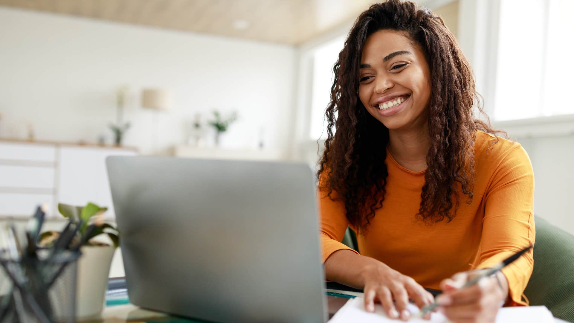 Woman smiling and writing in notebooks at home.