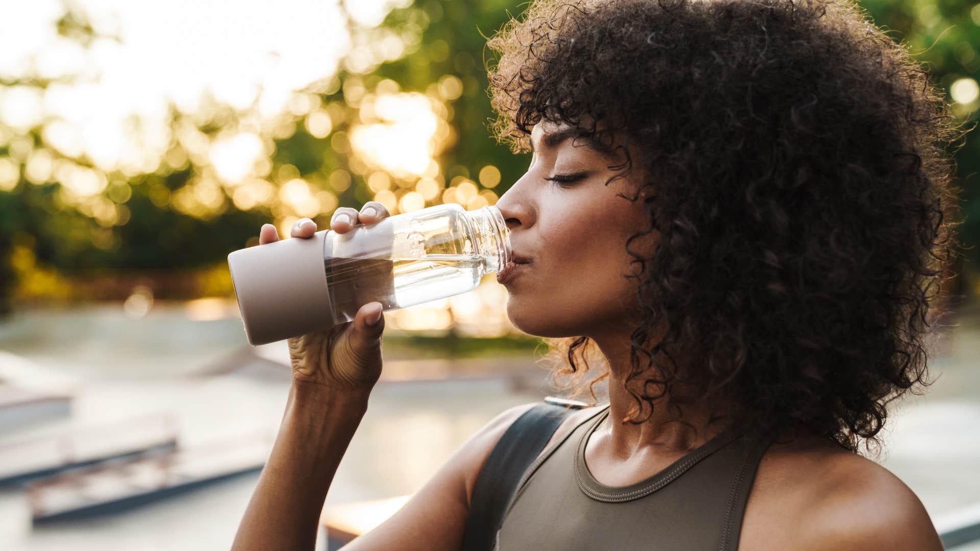 Woman drinking from a reusable water bottle outside.