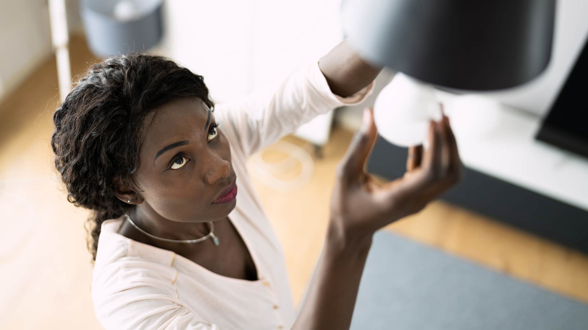 frugal woman replacing burned out light bulb in her home
