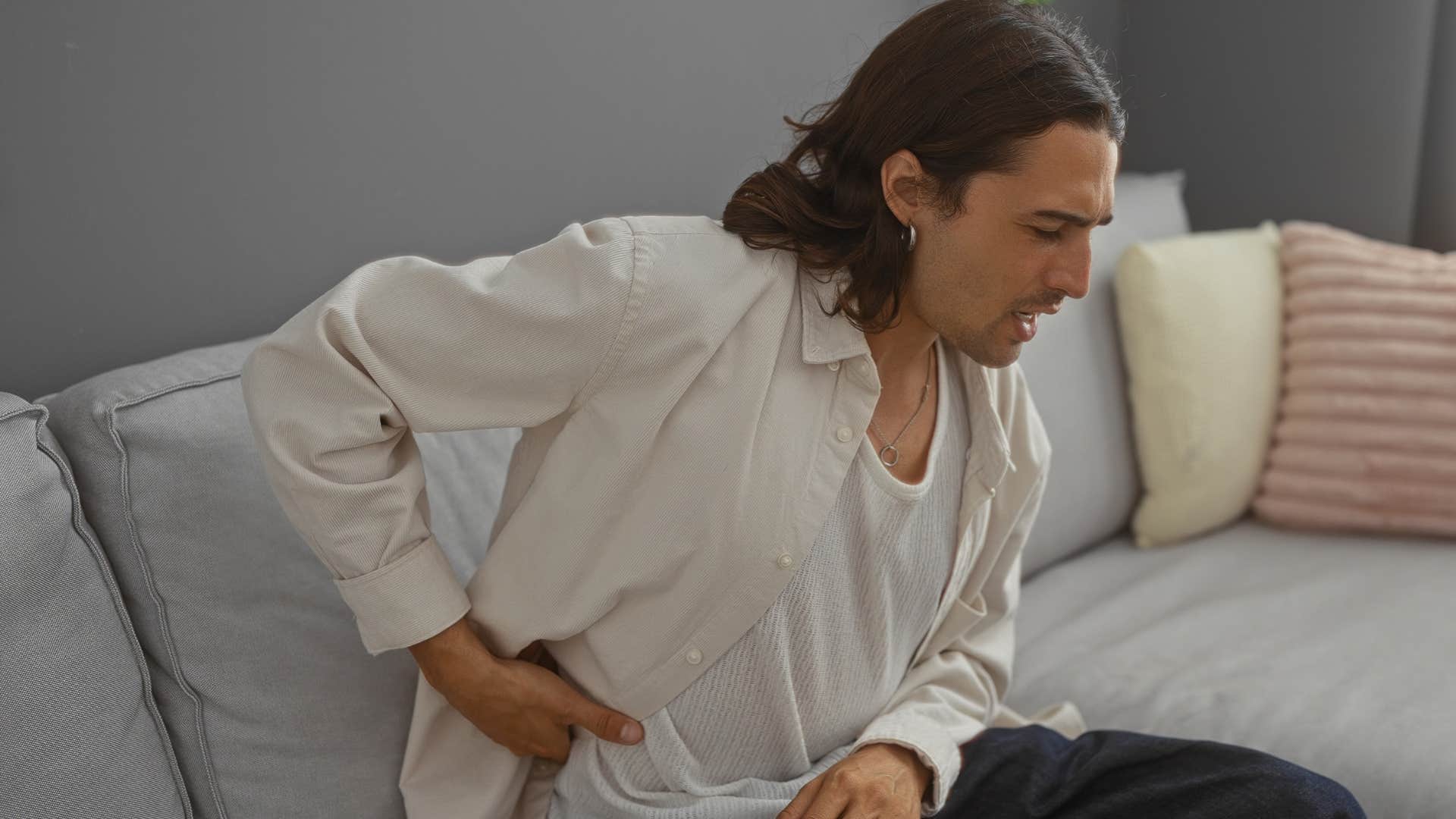man holding his back on uncomfortable furniture
