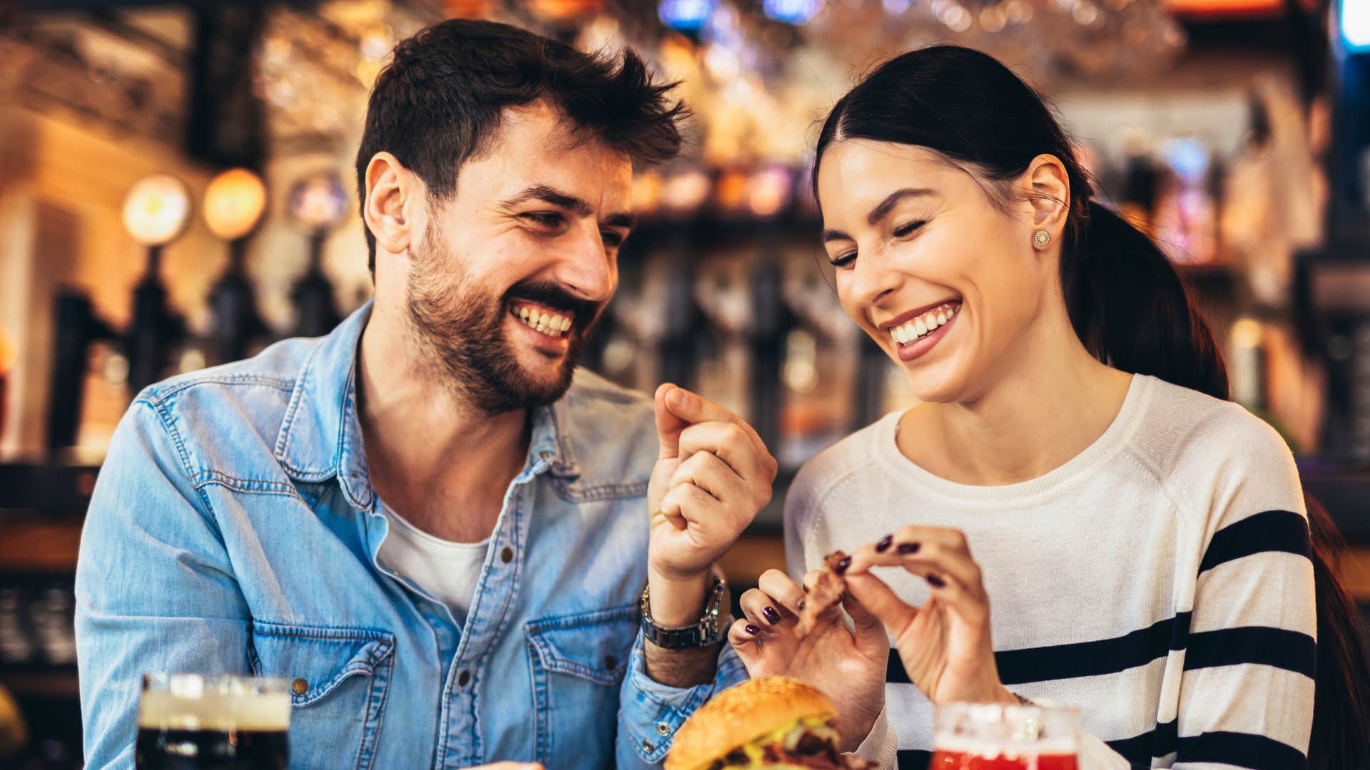 man and woman dining out regularly as they enjoy burger and soda together while smiling