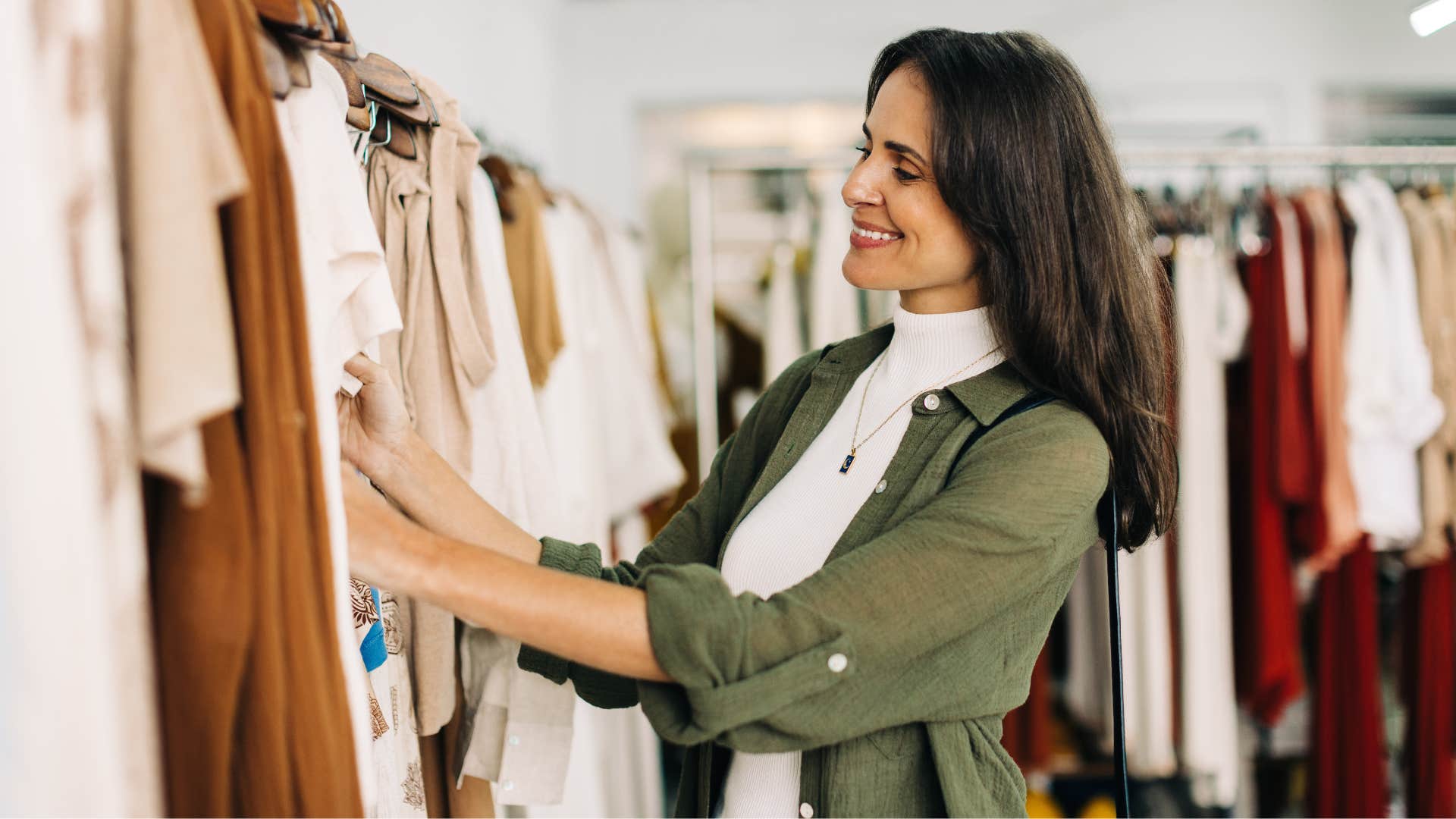 woman in green jacket looking through full price clothing as she smiles