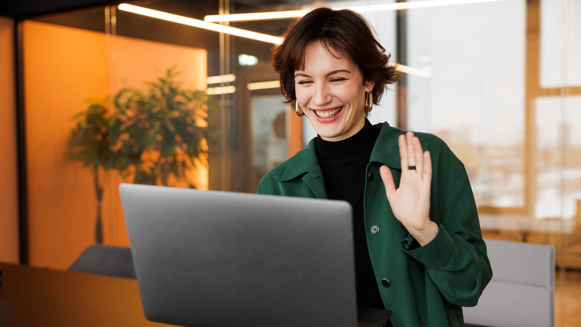 woman in green jacket waving and saying gen z slang