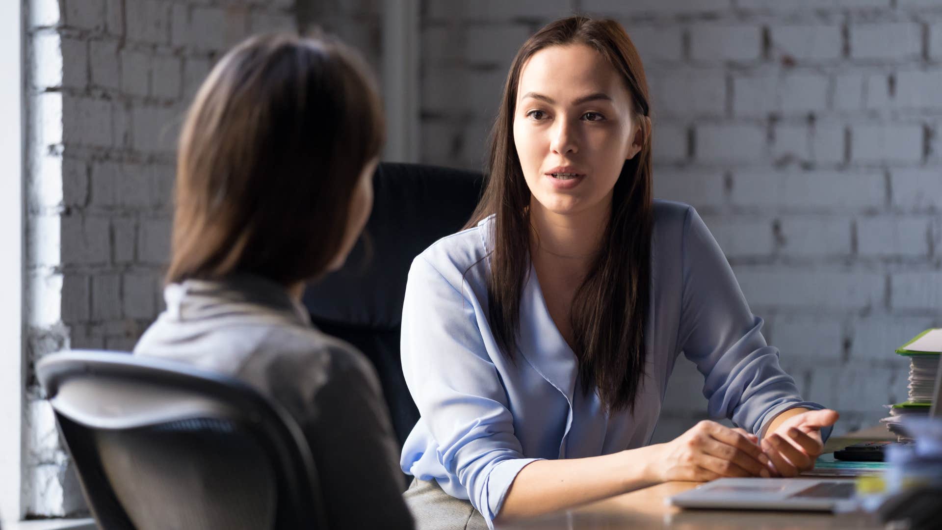 woman in blue shirt telling coworker this system is outdated as they sit across from one another