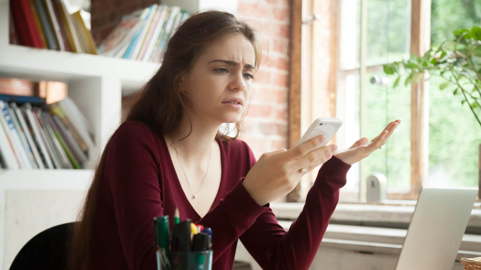 woman in red shirt annoyed as she stares at phone and thinks this could've been an email