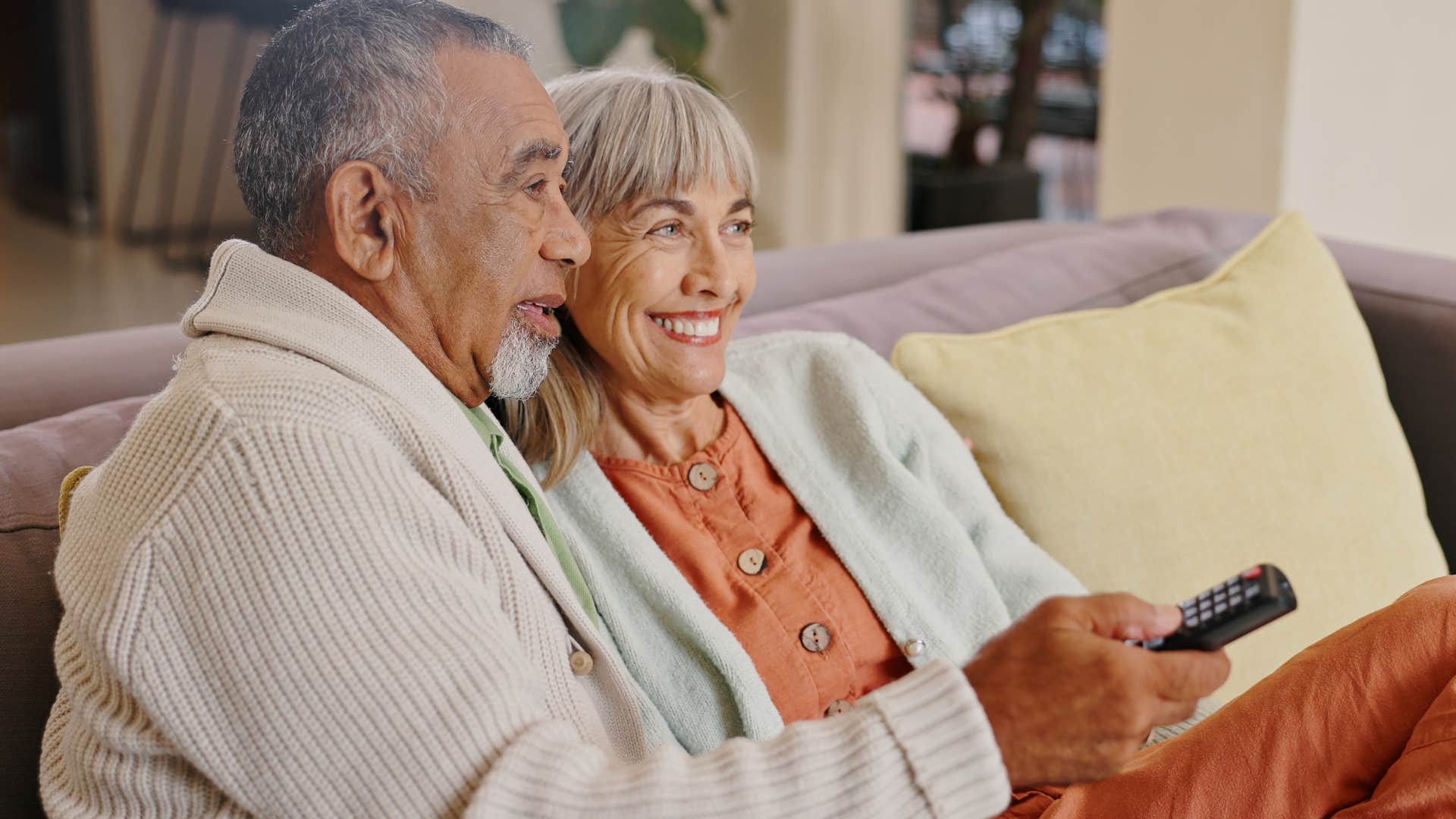 Older couple smiling and watching cable tv at home.